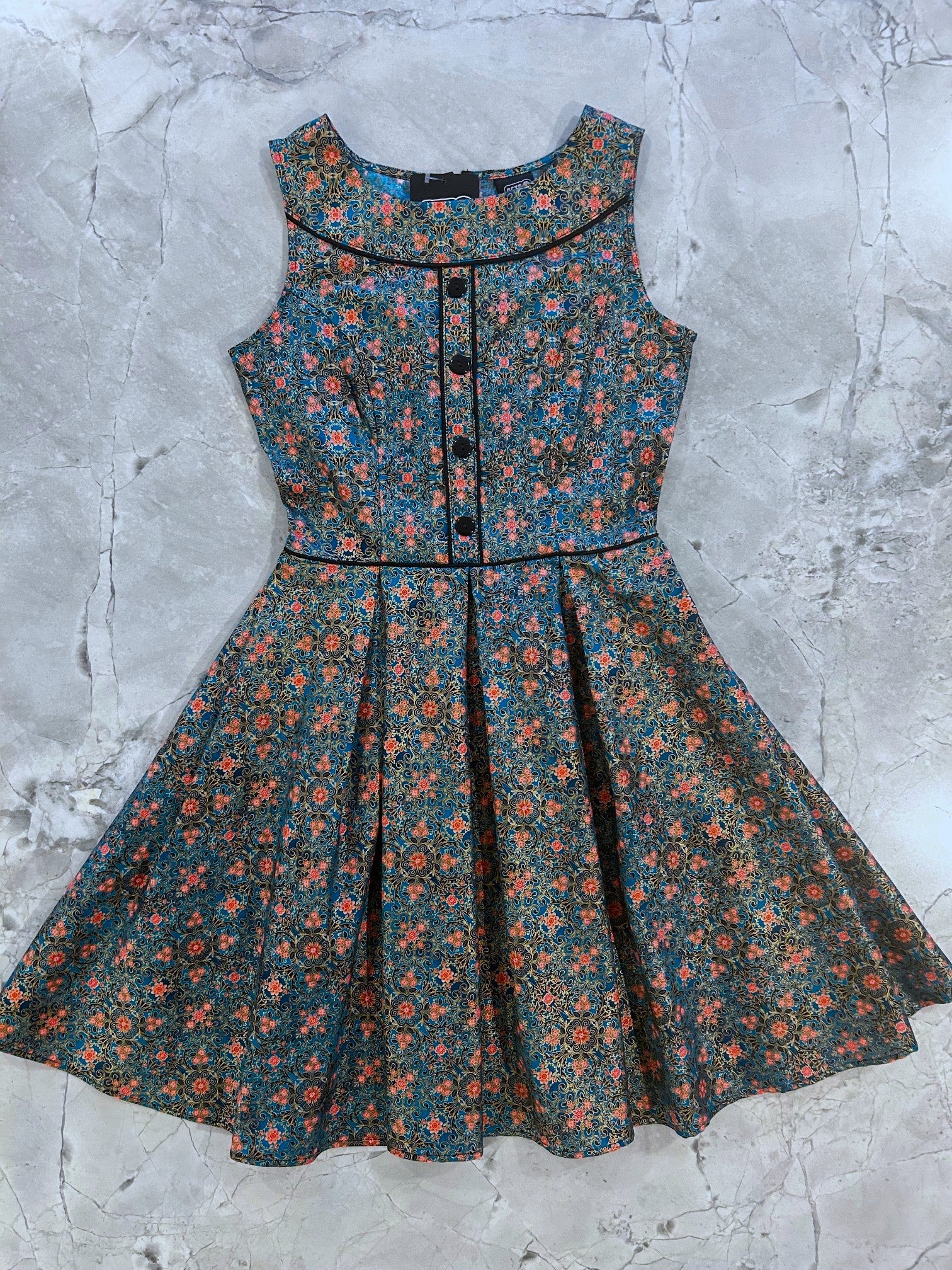 flatlay of Elizabeth dress in teal serenity print with gold accents and black piping and buttons